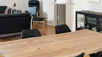 A modern living room with a wooden dining table, black chairs, a black sofa, a blue patterned armchair, and a white floor lamp.