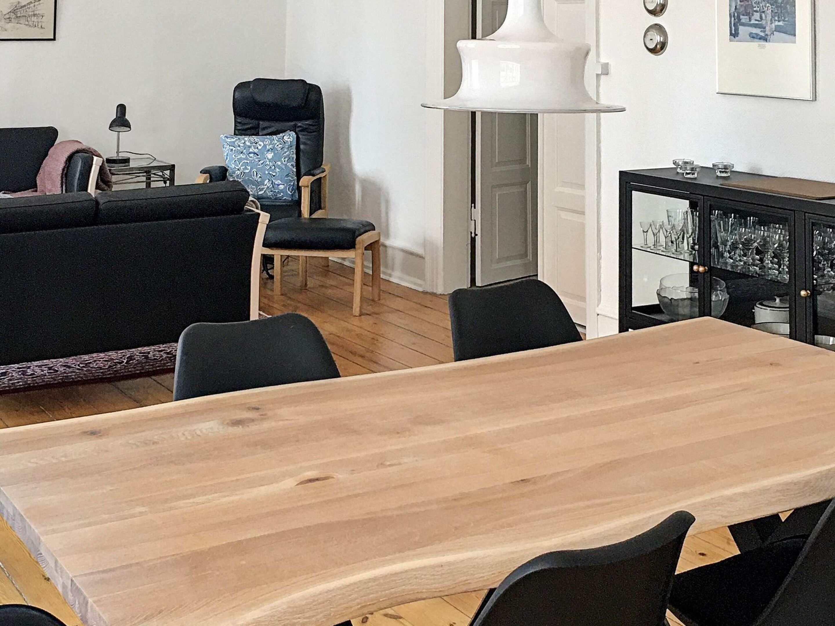 A modern living room with a wooden dining table, black chairs, a black sofa, a blue patterned armchair, and a white floor lamp.