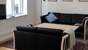 A living room with a black sofa, a wooden coffee table, and a floor lamp. There are three framed artworks on the wall. - 5 Star Holiday Home in Nakskov (Nakskov)