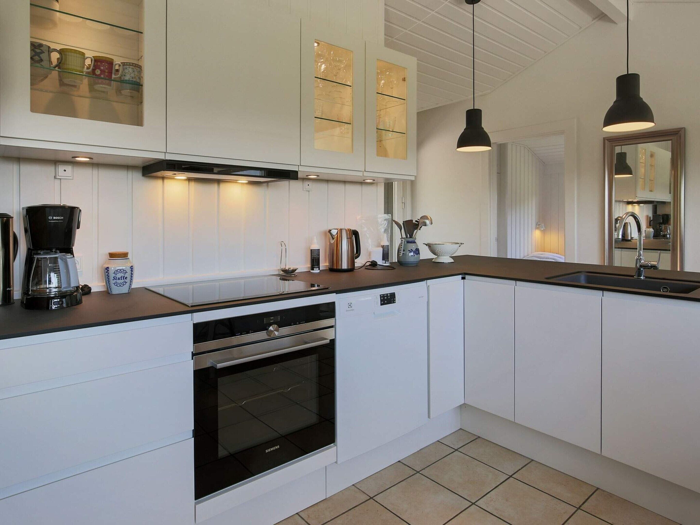 A modern kitchen with white cabinetry, a built-in oven, a coffee maker, and pendant lighting.