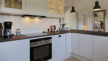 A modern kitchen with white cabinetry, a built-in oven, a coffee maker, and pendant lighting.