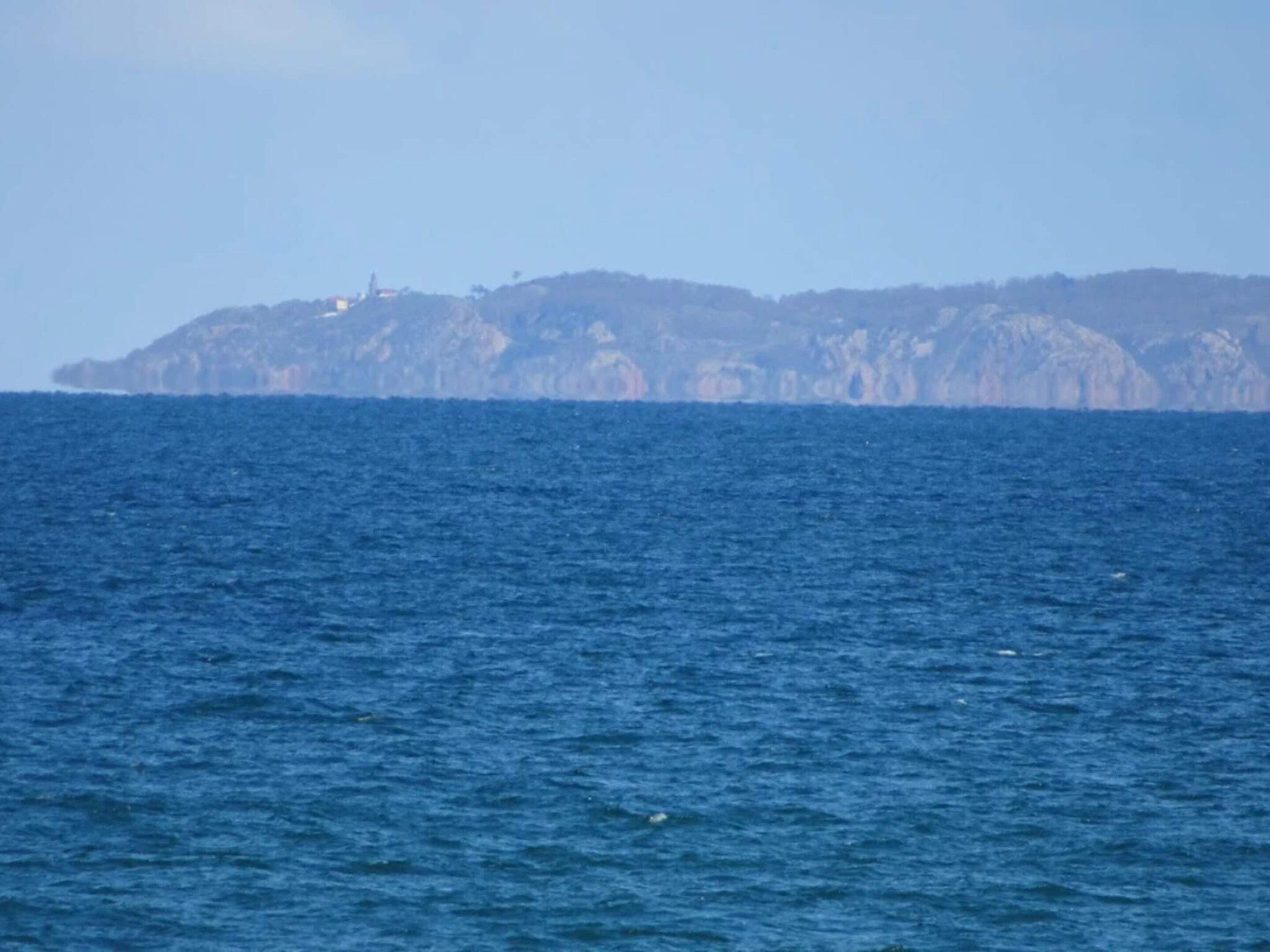 A coastal view with a rocky island in the distance and calm sea.