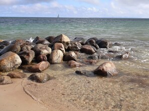 A rocky shoreline with clear water and a distant sailboat. - 4 Person Holiday Home in Gilleleje (Gilleleje)