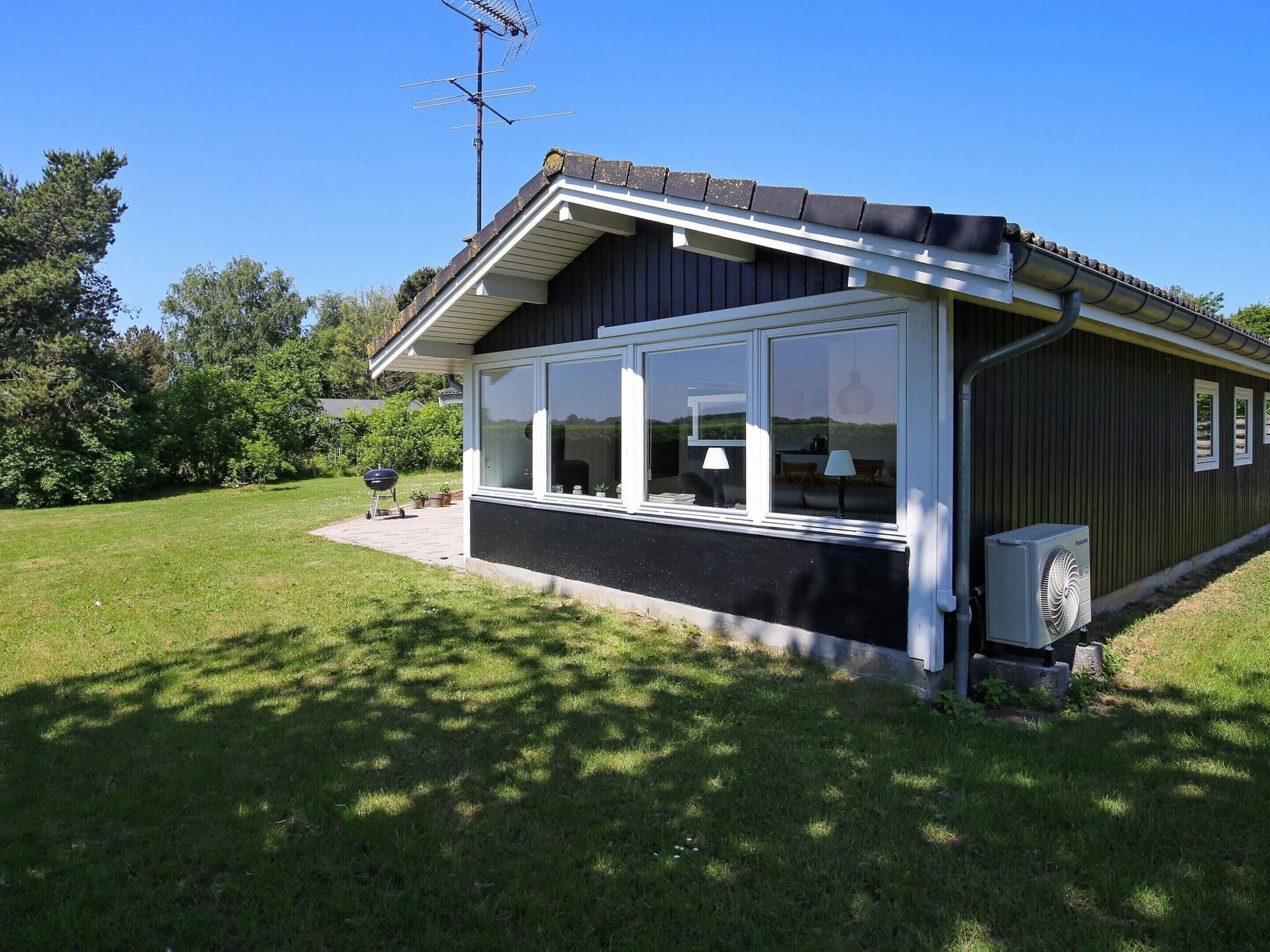 A single-story building with a large windowed porch, a satellite dish, and an air conditioning unit.