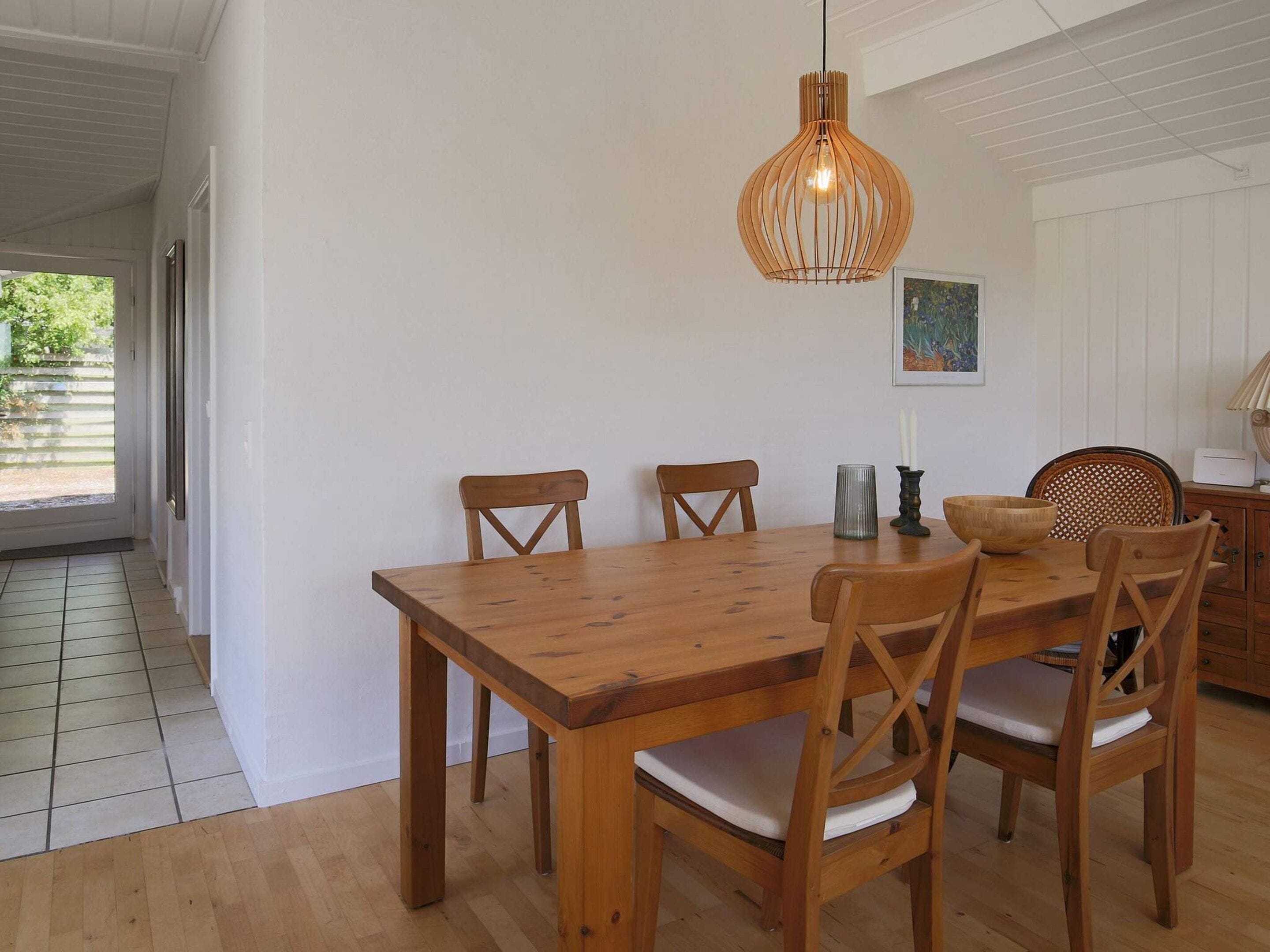 A dining area with a wooden table and chairs, a hanging light fixture, and a painting on the wall.