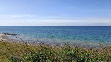 A coastal view with a sandy beach, clear blue sea, and distant sailboats.