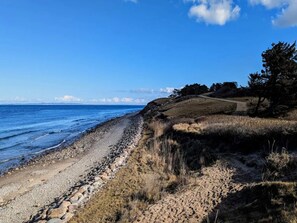 A coastal landscape with a pebble beach, grassy terrain, and a clear sky. - 4 Person Holiday Home in Gilleleje (Gilleleje)
