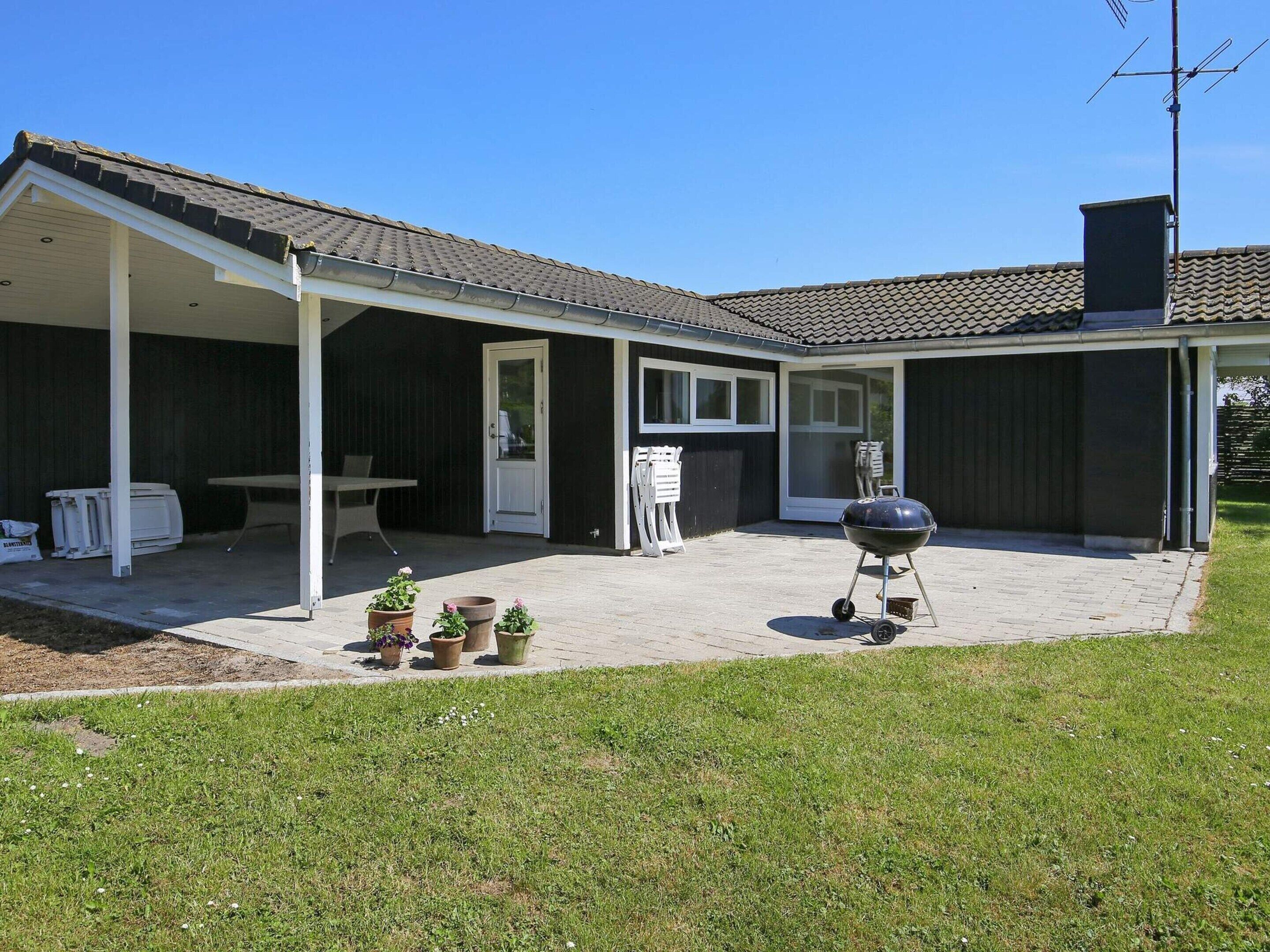 A covered patio with a grill, outdoor seating, and potted plants.