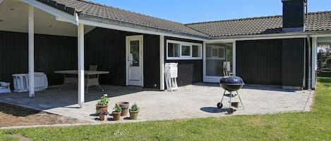A covered patio with a grill, outdoor seating, and potted plants.