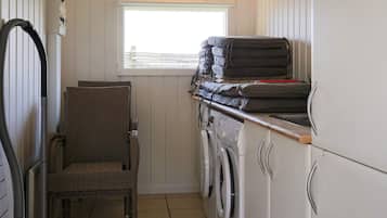 A compact laundry room with a washing machine, a chair, and a window.