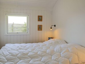 A bedroom with a large bed, a window with blinds, two wall-mounted picture frames, and a bedside table with books. - 4 Person Holiday Home in Gilleleje (Gilleleje)
