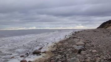 Una playa rocosa con olas, cielo nublado y una tierra firme a lo lejos.