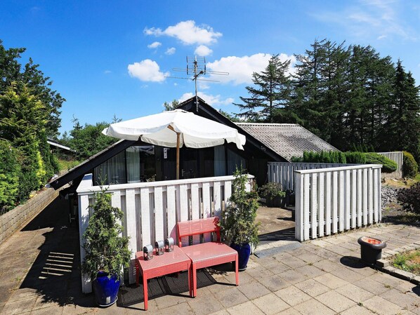 A cozy outdoor seating area with a red bench and a white umbrella, surrounded by potted plants and a wooden fence.