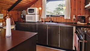 Une cuisine de taille réduite avec des murs en bois, une fenêtre et les appareils de base, notamment un four à micro-ondes, un évier et une cuisinière.