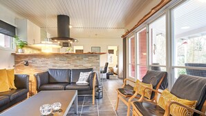A modern living room with a fireplace, a dining area, and large windows offering a view of the outdoors. - 4 Person Holiday Home in Aakirkeby (Akirkeby)