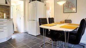 A compact kitchen with a refrigerator, microwave, and a dining area with a table and chairs. - 4 Person Holiday Home in Aakirkeby (Akirkeby)
