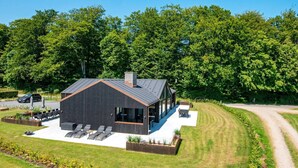 A modern house with a sloped roof, a covered patio with seating, and a well-maintained lawn. - 12 Person Holiday Home in Haderslev (Haderslev)