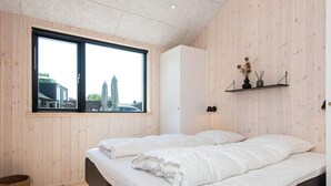 A bedroom with two beds, a large window, wooden walls, and a small shelf with decorative items. - 12 Person Holiday Home in Haderslev (Haderslev)