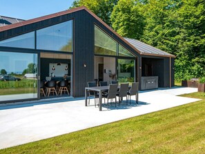 A modern house with large glass windows, a dining area with outdoor seating, and a garage. - 12 Person Holiday Home in Haderslev (Haderslev)