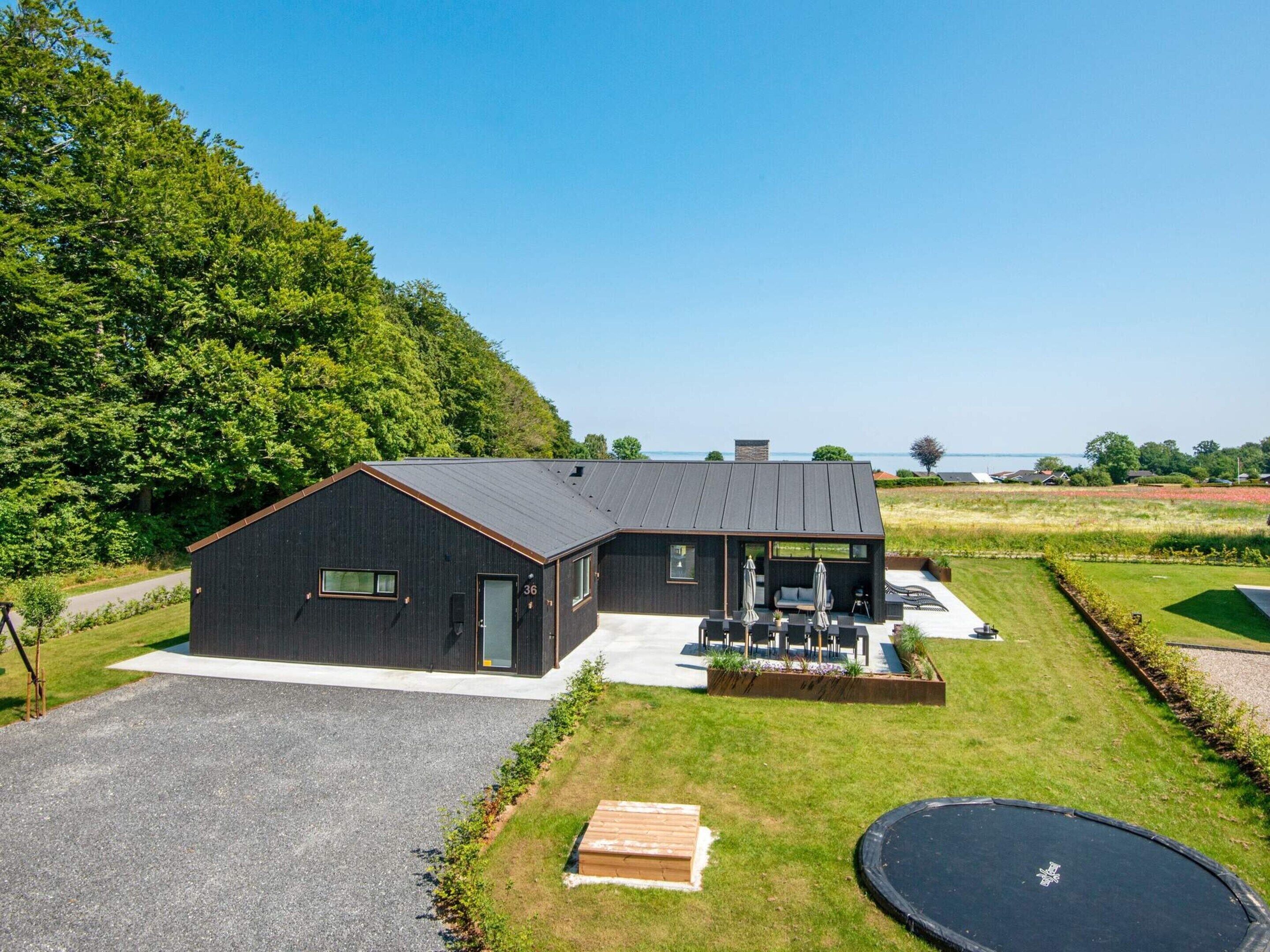 A modern black house with a patio, a trampoline, and a view of the sea.