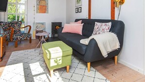 Un salon chaleureux avec un canapé foncé, un pouf vert, une petite table ronde et une cheminée.