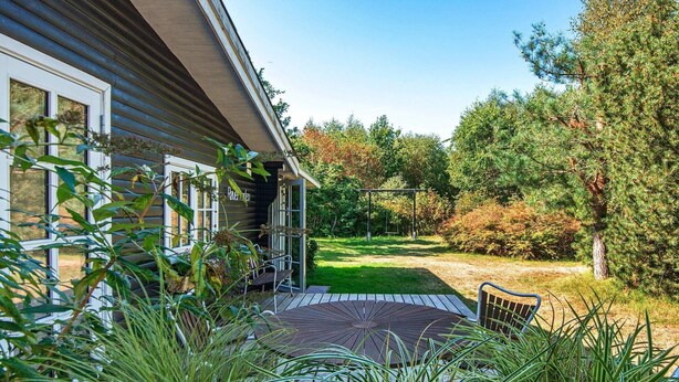 Une maison en bois avec une terrasse couverte et un portique avec des balançoires dans le jardin.