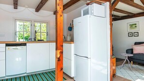 Une cuisine compacte avec des meubles blancs, un réfrigérateur blanc et une structure en poutres apparentes.