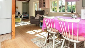 Une cuisine chaleureuse avec des poutres en bois, une table à manger recouverte d’une nappe rose et un réfrigérateur blanc.