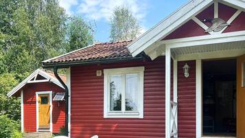 A red wooden cabin with a porch and a small attached structure, a table with chairs, and a door leading to the interior.