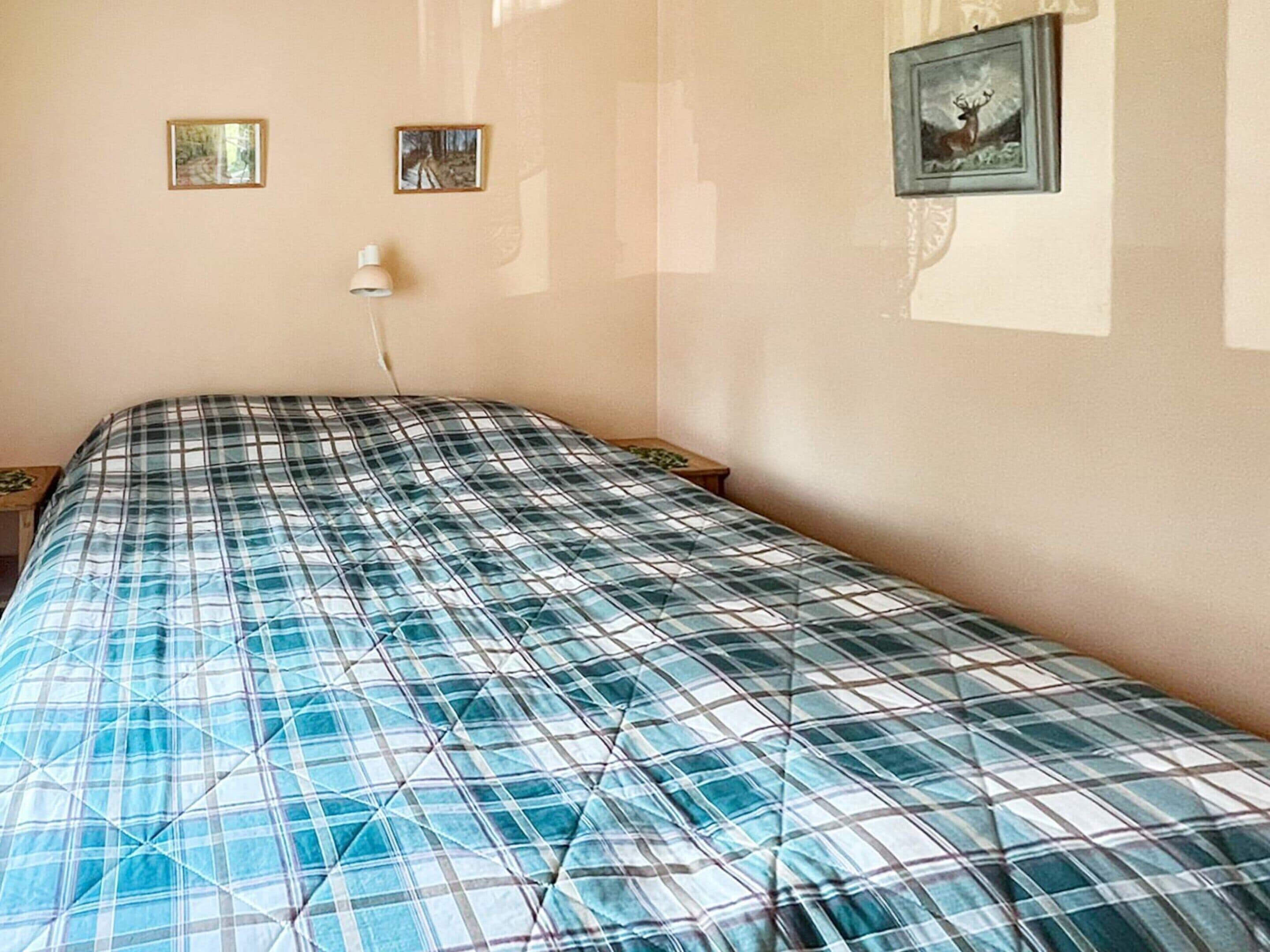 Un dormitorio con una cama, dos cuadros en la pared y una lámpara de noche.