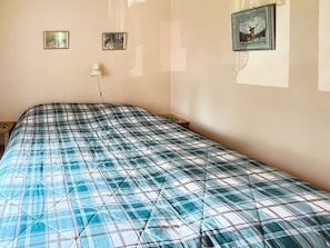 Quarto com cama, duas fotos emolduradas na parede e abajur.