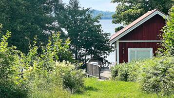 A red cabin with a deck overlooking a lake, surrounded by dense greenery.