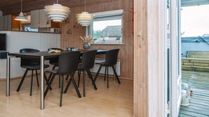 A modern kitchen with wooden walls, a dining area with black chairs, and pendant lights. - 6 Person Holiday Home in Ringkobing (Ringkobing)