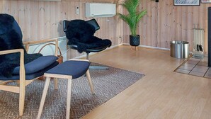 A modern living room with wooden walls, a skylight, a large potted plant, a black chair, a wooden coffee table, and a small TV. - 6 Person Holiday Home in Ringkobing (Ringkobing)