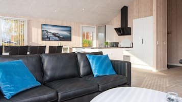 Een moderne woonkamer met een zwarte leren bank, een witte salontafel en een grote flatscreen televisie aan de muur.