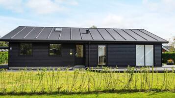 A modern two-story house with a dark exterior, large windows, and a flat roof.