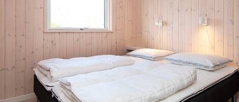Un lit double avec une literie blanche, dans une pièce aux murs en bois et dotée d’une fenêtre.