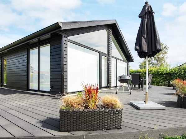A modern house with a deck, a barbecue grill, and outdoor furniture.