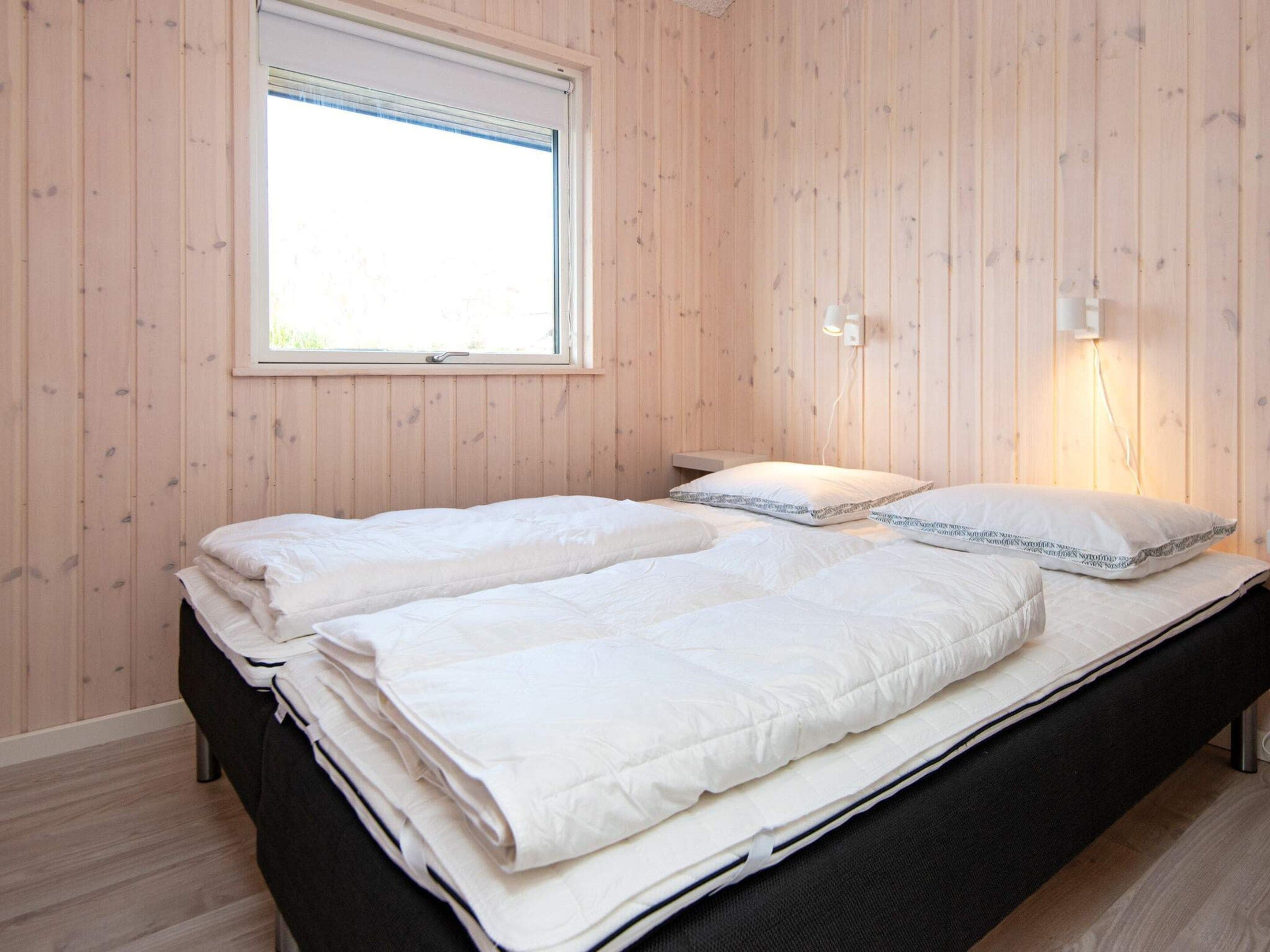 A bedroom with a bed, a window, and a wall-mounted light fixture.