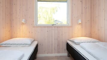 Quarto com duas camas, uma janela e luminária fixada na parede.