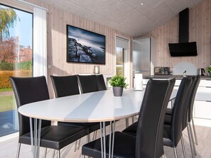 A modern dining area with a round table, black chairs, a potted plant, and a TV mounted on the wall. - 4 Star Holiday Home in Borkop (Borkop)