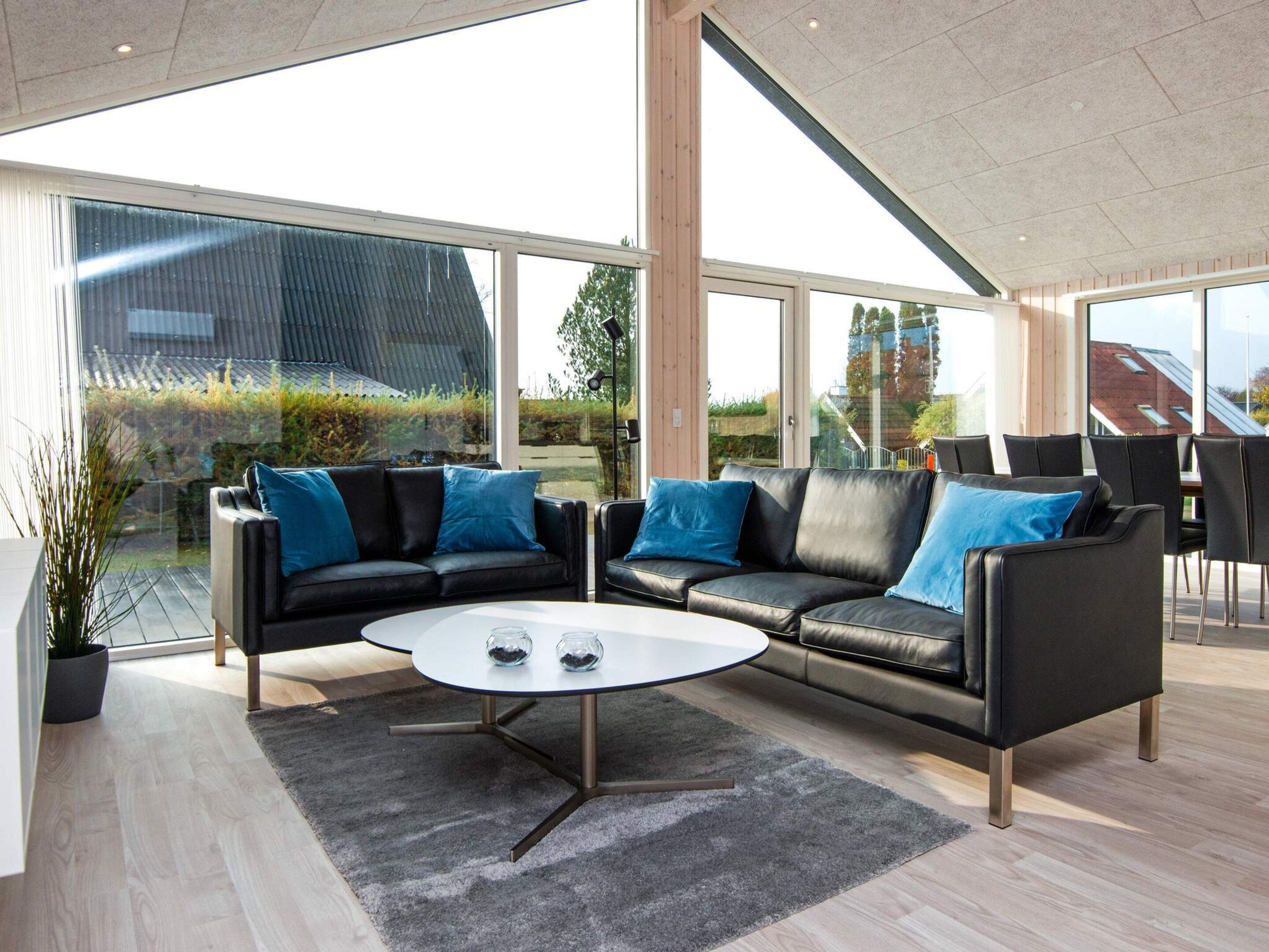 Ein modernes Interieur mit einer Eckcouch, einem runden Couchtisch und großen Fenstern mit Blick ins Freie.