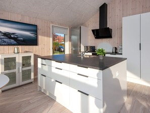 A modern kitchen with a large island, white cabinetry, and a black range hood.