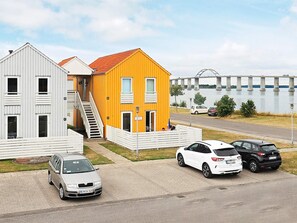 A residential area with a white building and a yellow house with a red roof, a bridge in the background, and three cars parked in front. - 4 Person Holiday Home in Rudkobing (Rudkobing)