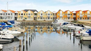 Marina com barcos atracados, uma parede de pedra e edifícios coloridos ao fundo.