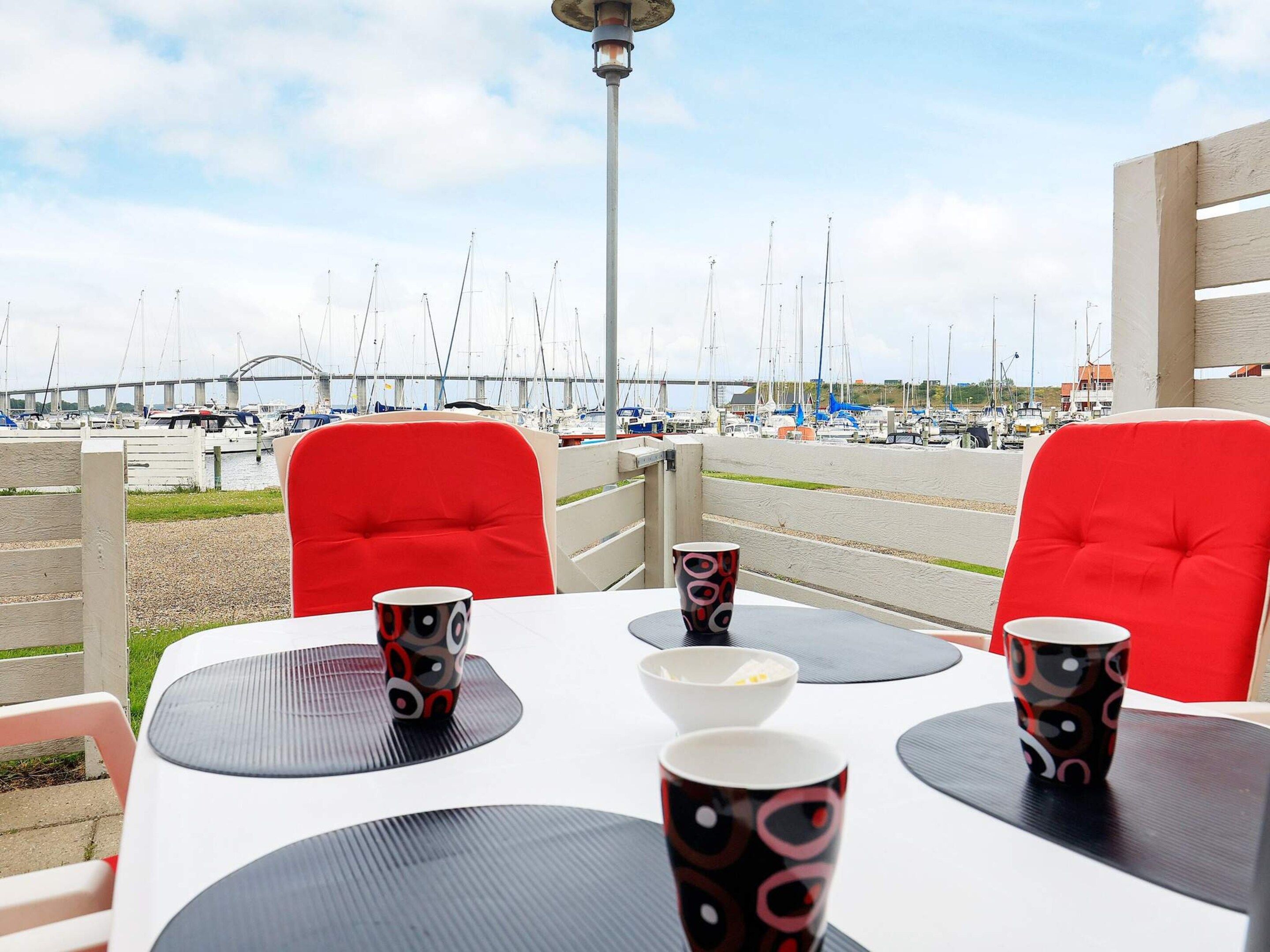 A dining area with tables and chairs, a view of a marina with boats, and a bridge in the background.