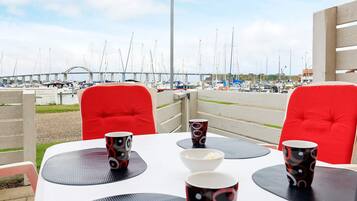 A dining area with tables and chairs, a view of a marina with boats, and a bridge in the background.