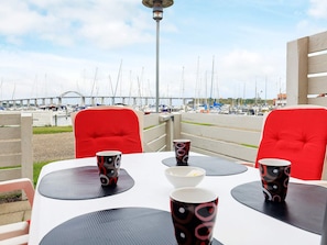 A dining area with tables and chairs, a view of a marina with boats, and a bridge in the background. - 4 Person Holiday Home in Rudkobing (Rudkobing)