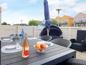 An outdoor dining area with a table set for two, a bottle of wine, and a bowl of fruit. - 4 Person Holiday Home in Rudkobing (Rudkobing)