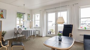 Quarto de hotel moderno com área de jantar, uma grande janela com vista e um espaço de estar com mesa e cadeiras.